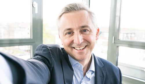Jean-Marc Noel, CEO von Trusted Shops, lächelt in die Kamera und macht in seinem Büro ein Selfie.